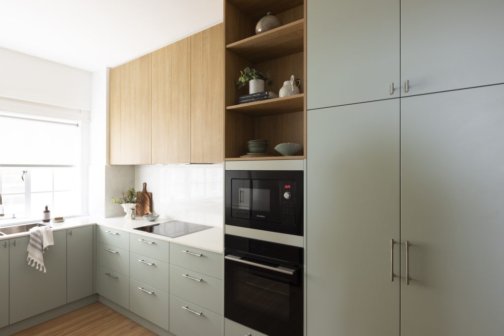Modern kitchen in an Elizabeth Bay flat with pale green base cupboards, wood-toned wall cupboards, a built-in oven and microwave, and white worktops.