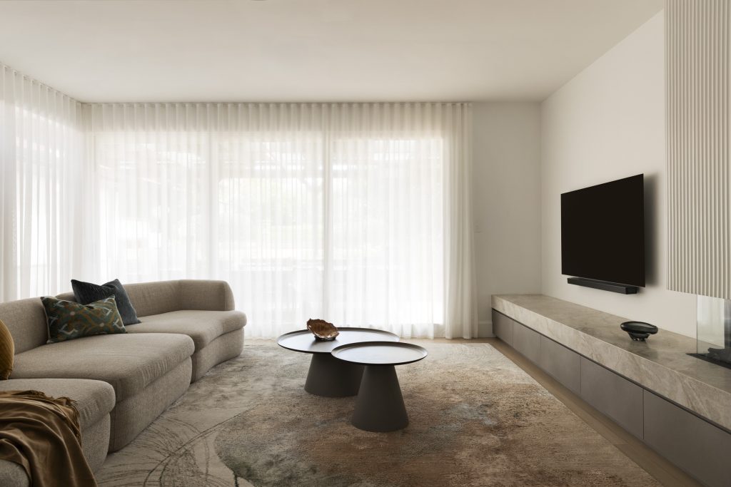 A beige corner sofa, stacked circular coffee tables, and a wall-mounted television above a stone-topped media unit in this Californian bungalow renovation.